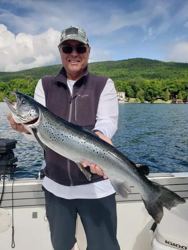 Man holding a large Salmon on a boat with green hills in the background
