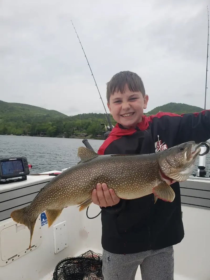 Boy smiling and holding a large Lake Trout on a boat