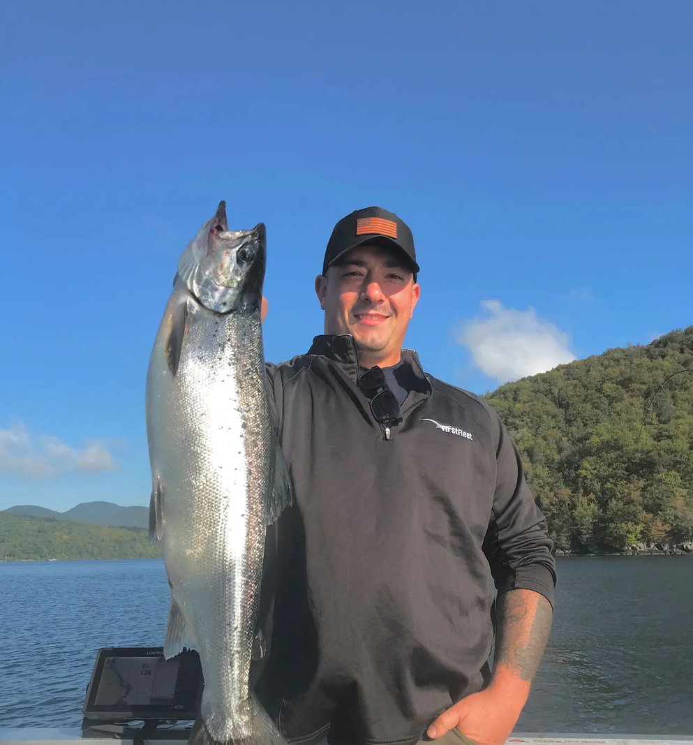Man holding a large Salmon against a clear blue sky and green hills