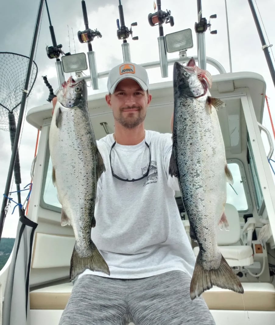 Man holding two large Salmon on a boat with fishing rods in the background