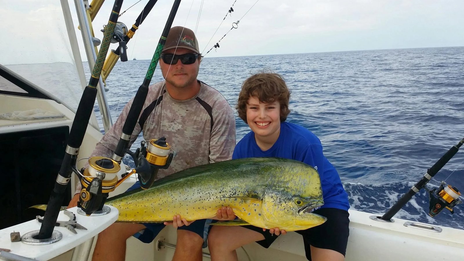 Two anglers on a boat holding a large mahi-mahi.