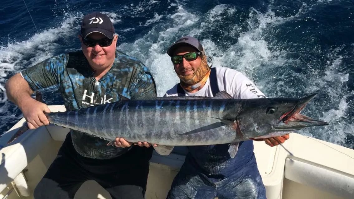 Two anglers on a boat holding a large wahoo.