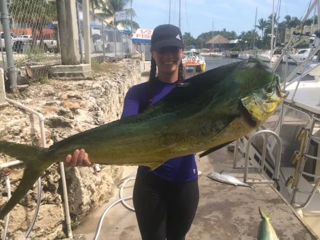 Woman on a dock holding a large mahi-mahi.
