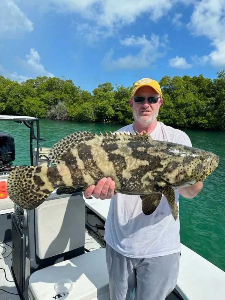Angler smiling while holding a juvenile tarpon in the water at sunset.