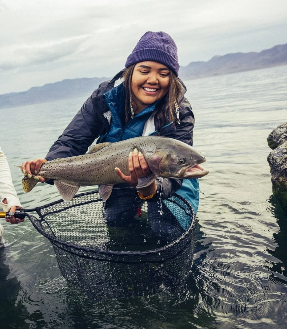 Smiling angler holding a large Cutthroat Trout over a landing net in the water.