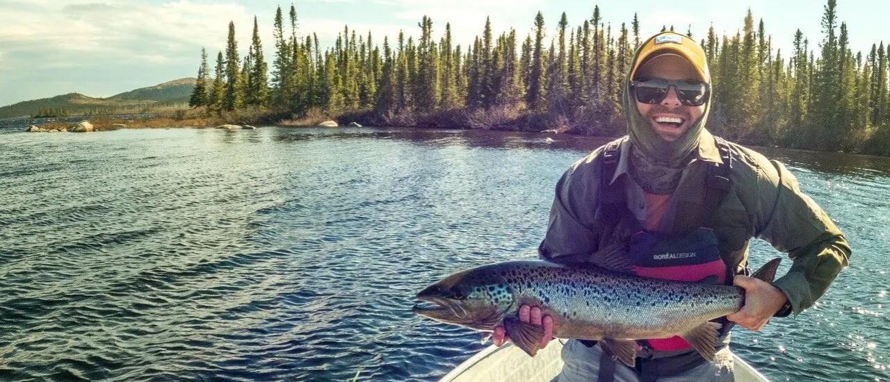 Man in sunglasses holding a large speckled fish in a boat on a lake.