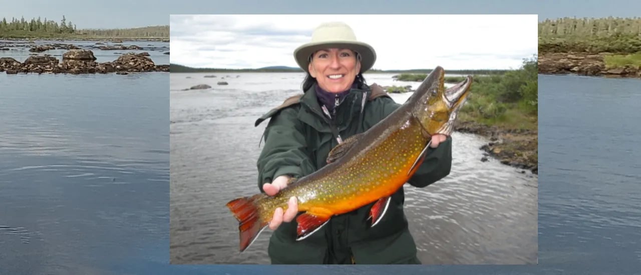 Woman in a hat holding a large orange-bellied fish in a river.