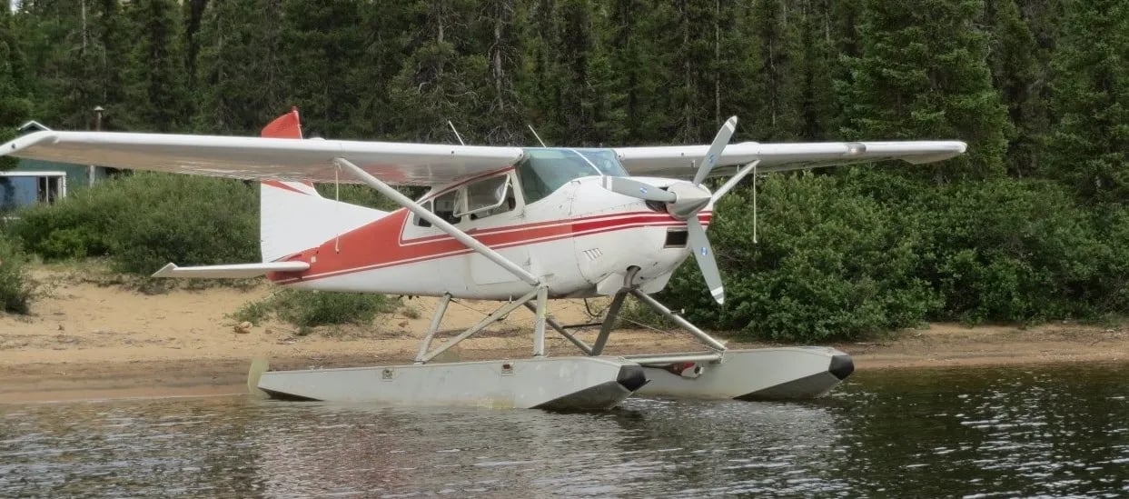 Red and white floatplane docked on a calm lake surrounded by trees.