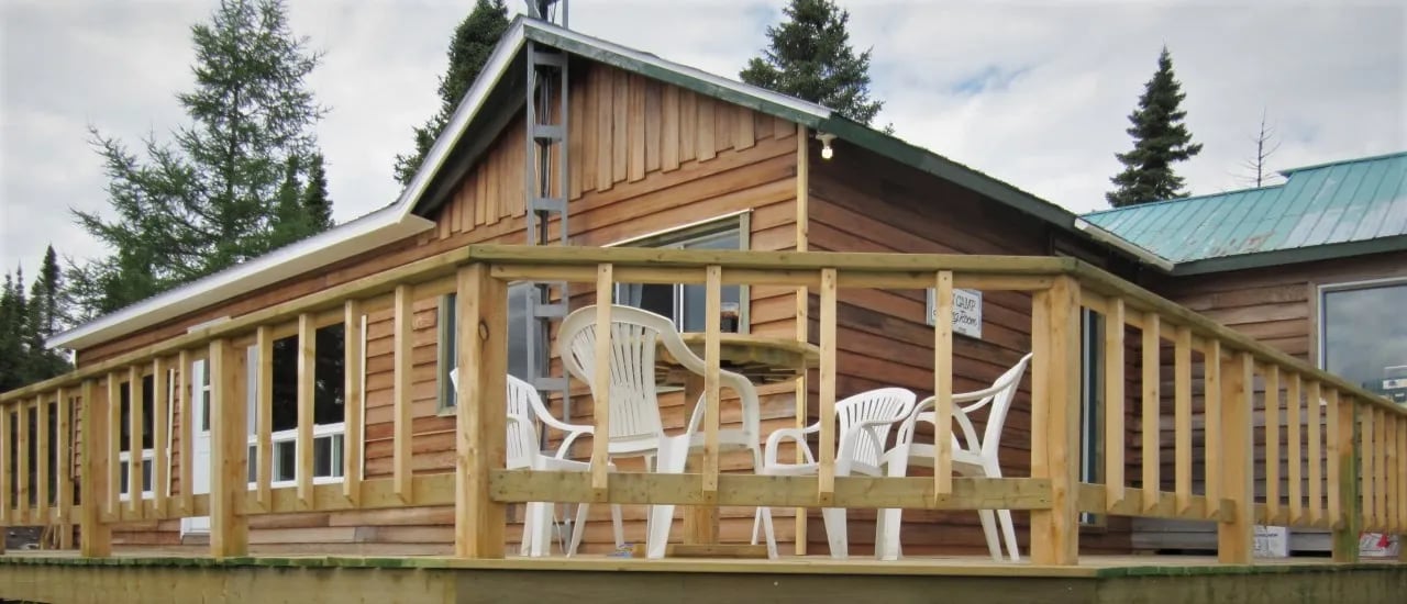 Wooden lodge with a spacious deck and white patio furniture.