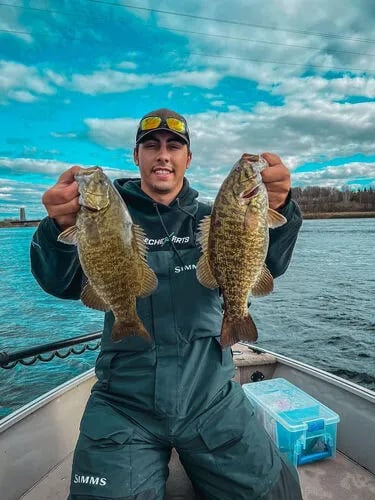 Angler on a boat holding two large smallmouth bass against a blue sky