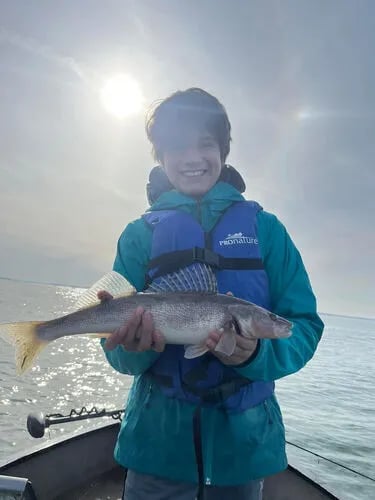 Young angler in a life vest holding a walleye on a boat under bright sunlight