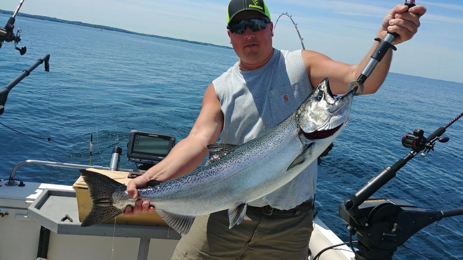 Angler on a boat holding a large Lake Trout with blue water in the background.