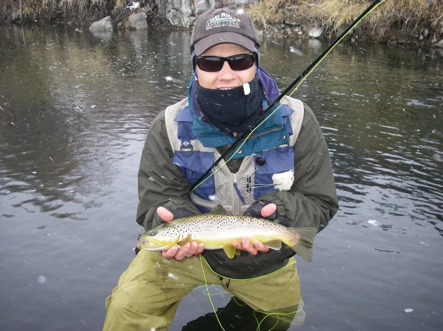 Group of anglers smiling and holding a Brown Trout in a snowy river.