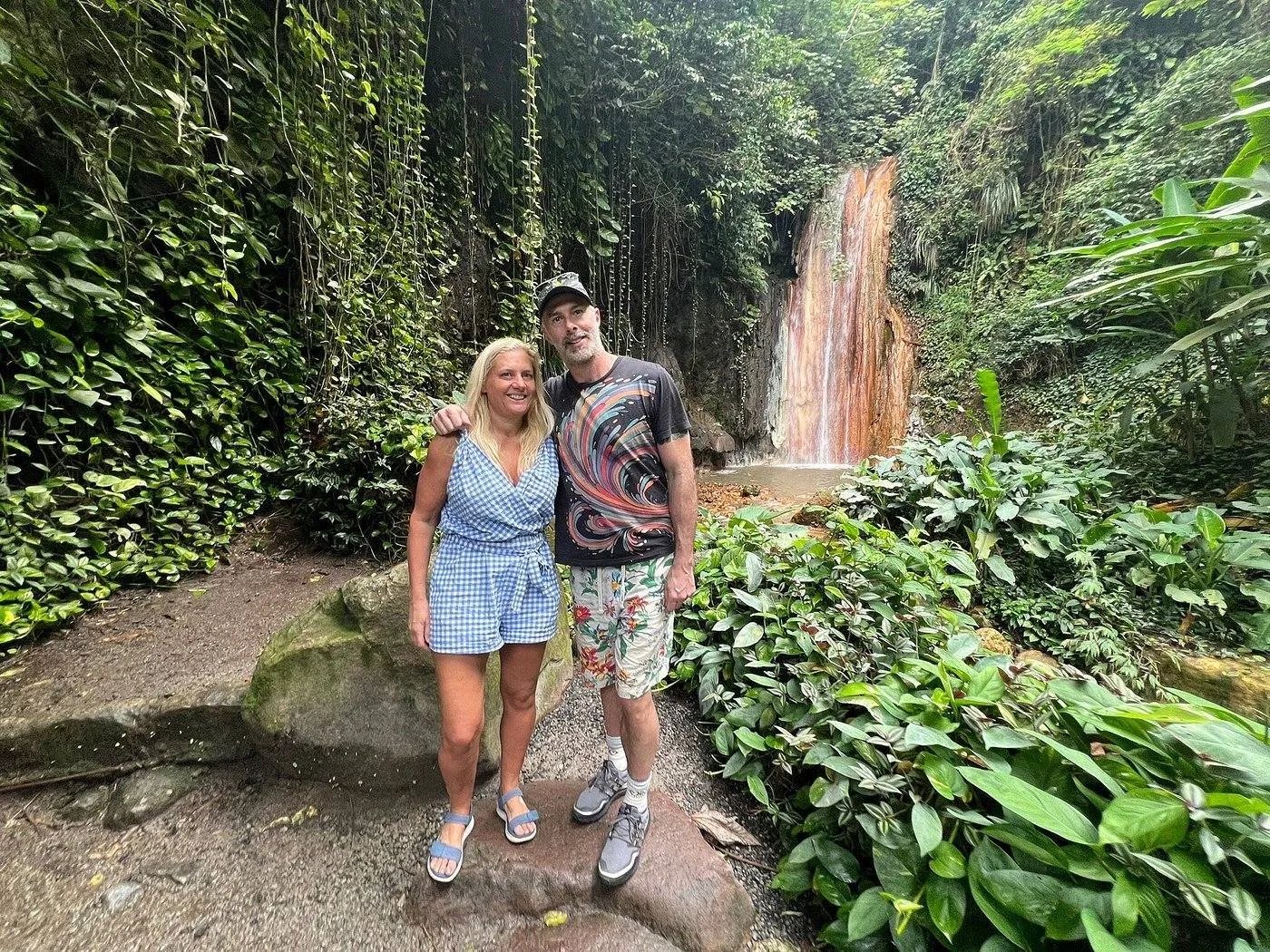 Couple posing in front of a natural waterfall in a lush green forest