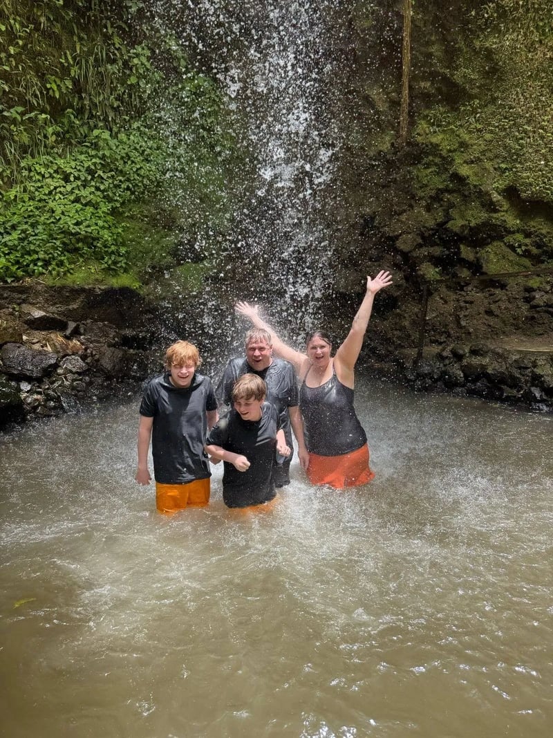 Family of four standing under a powerful waterfall, splashing in the water