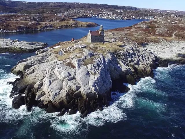 Lighthouse on a rocky island surrounded by ocean under a grey sky.
