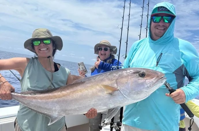 Two anglers holding a large Amberjack on a boat with another person in the background