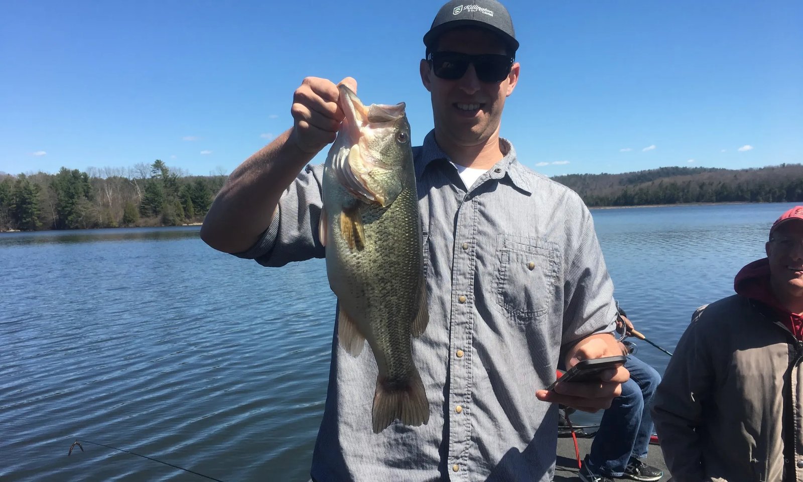 Angler on a boat holding a large Largemouth Bass with a lake in the background