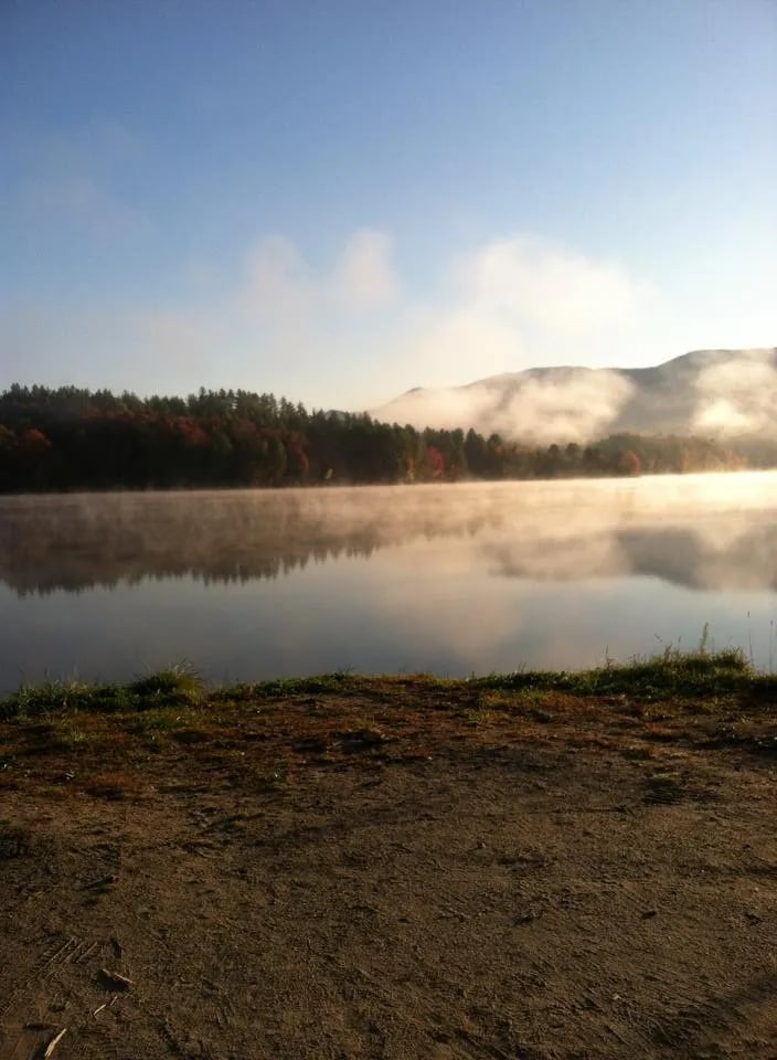 Misty morning over a calm lake with forested shores and a distant mountain
