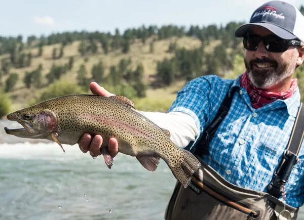 Chris Wells smiling while holding a Rainbow Trout in a river