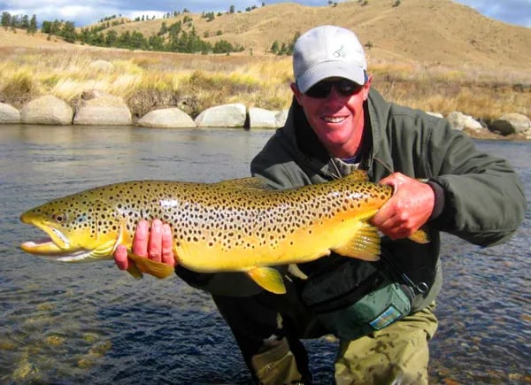 Matt Thomas smiling while holding a large Brown Trout in a river