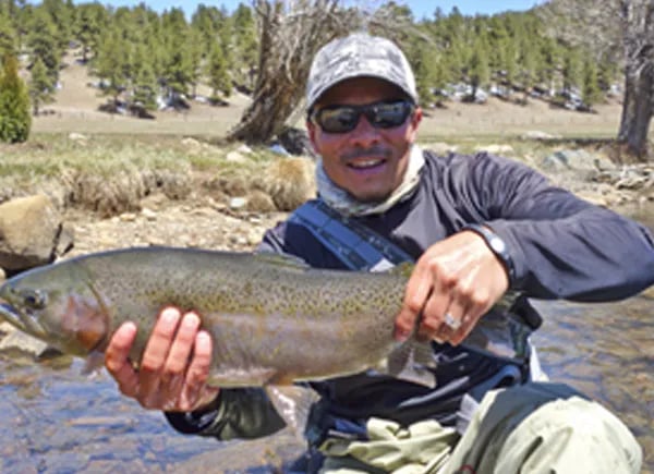 Jeremy Clements smiling while holding a large Rainbow Trout in a river