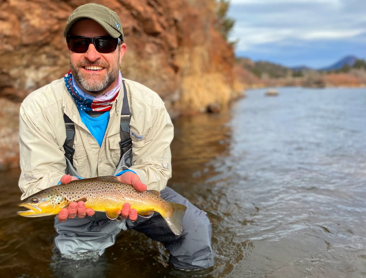 Chris Wells smiling while holding a Brown Trout in a rocky river