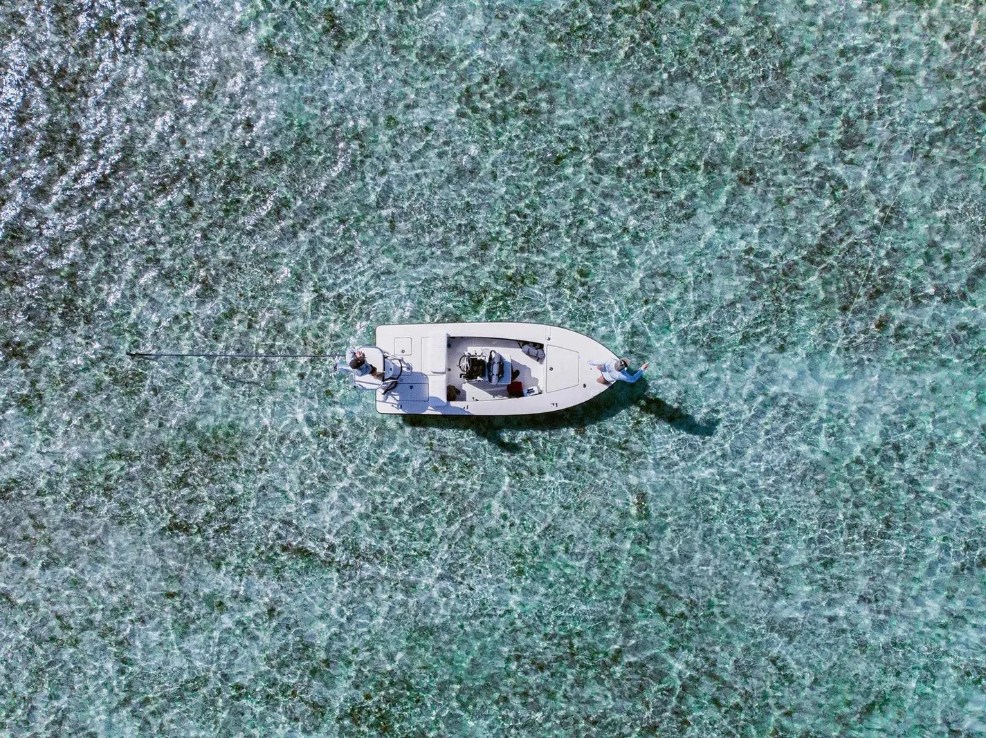 Aerial view of a flats boat in clear turquoise water.