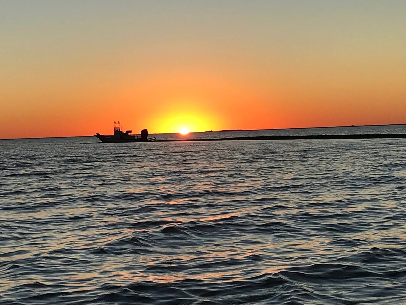 Boat silhouette on the horizon at sunset over calm water