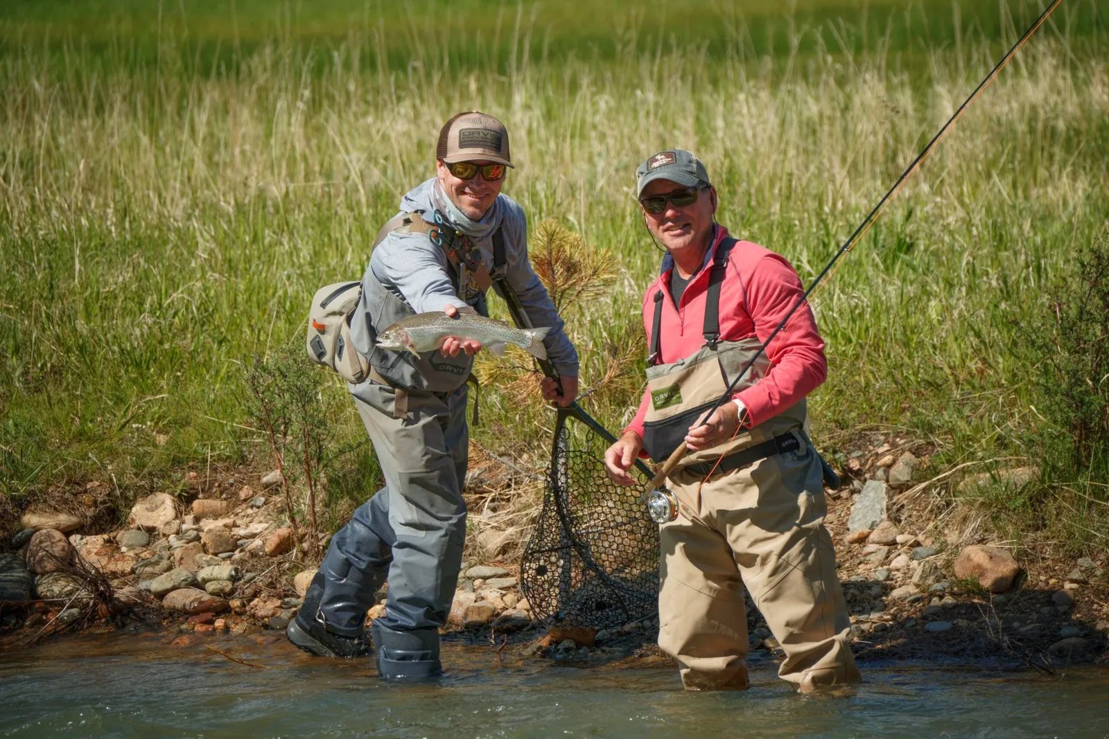 Two anglers in a river, one holding a fish and smiling