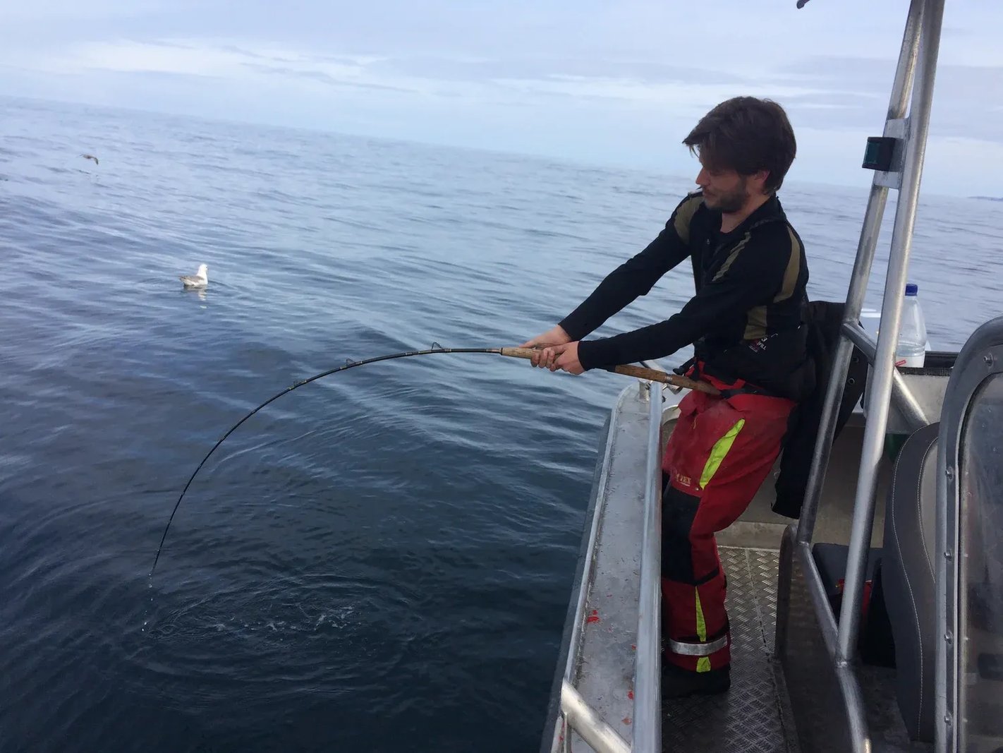 Angler in red and black gear fighting a fish from a boat.