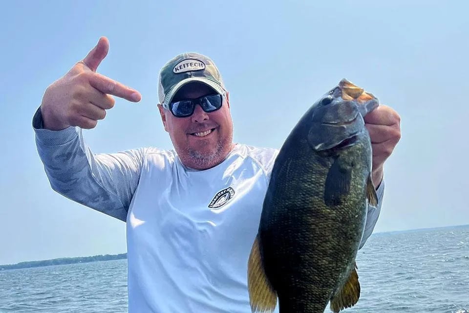 Angler in sunglasses holding two large Smallmouth Bass on a boat