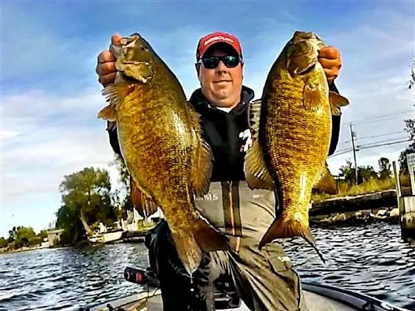 Angler in a life vest holding a Smallmouth Bass on a boat, another angler in the background