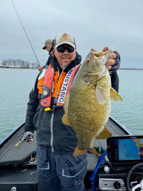 Two anglers smiling and holding Smallmouth Bass on a boat