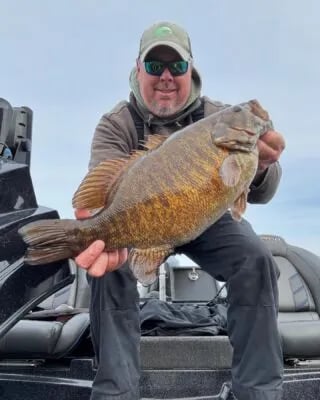 Angler in sunglasses holding a Smallmouth Bass and pointing to it on the water