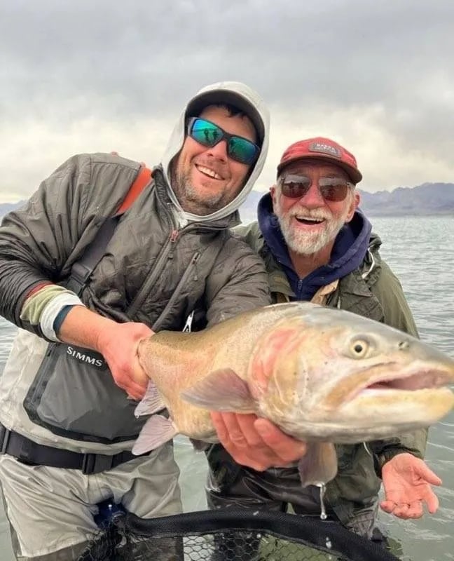 Two anglers holding a large Brown Trout in a river.