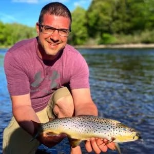 Angler smiling while holding a large King Salmon in a river with green foliage