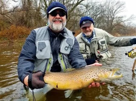 Angler in a yellow jacket holding a large Brown Trout in a river.
