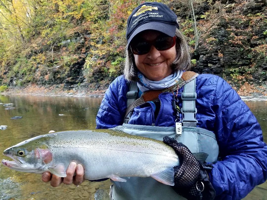 Angler holding a Steelhead in a river with autumn foliage.