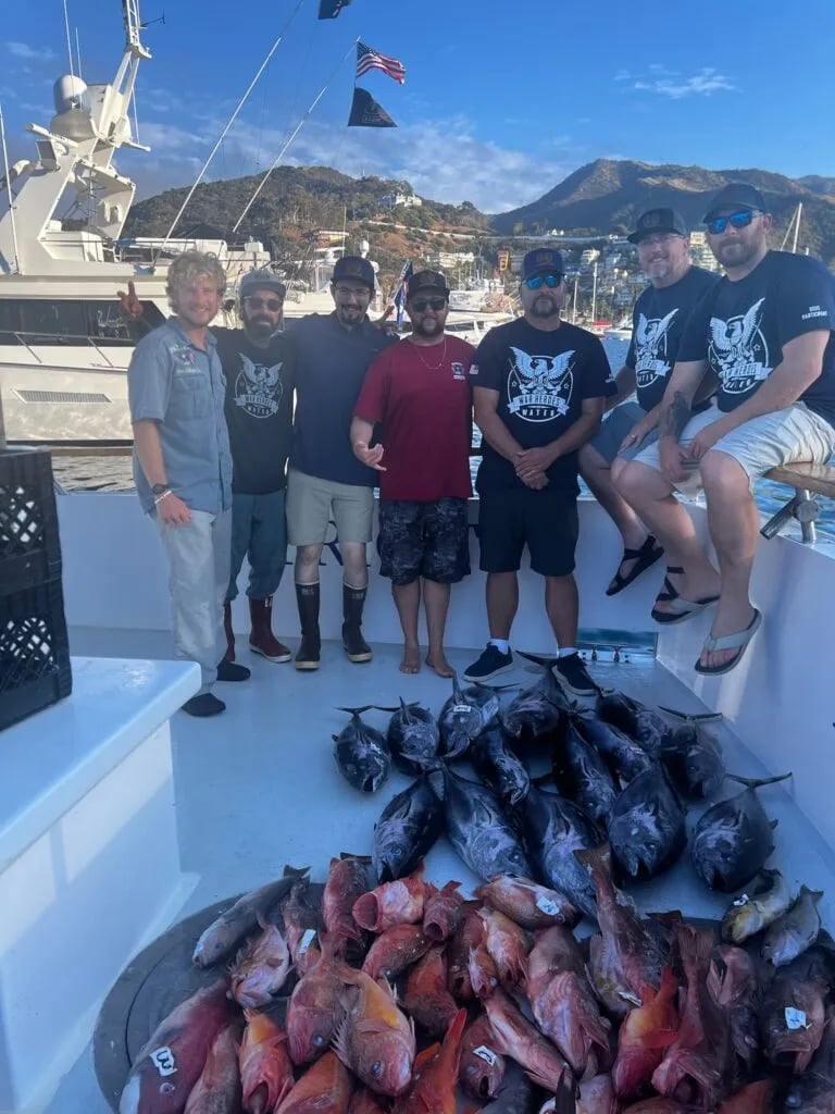 Group of anglers on a boat deck with a large pile of various fish.