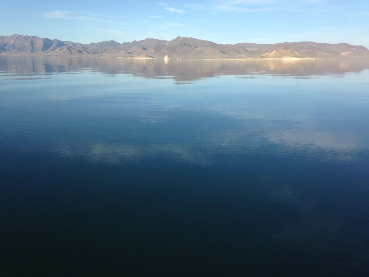 Calm lake water reflecting mountains and a clear blue sky.