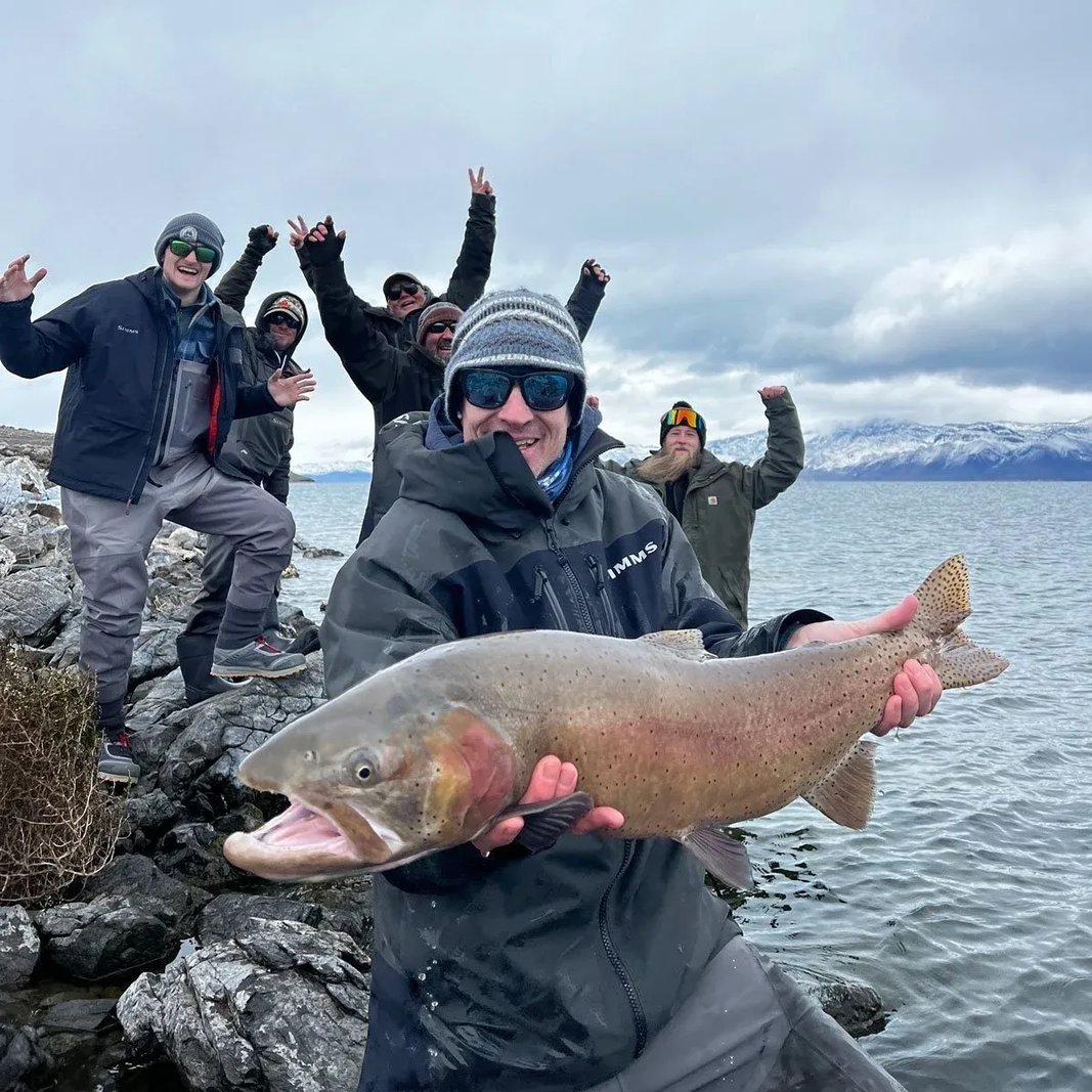 Group of excited anglers on a rocky shore celebrating a large Cutthroat Trout.