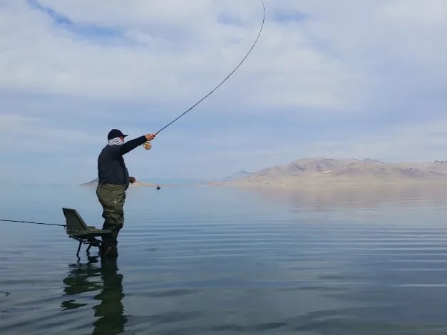 Two anglers fishing from a white center console boat on a calm lake with mountains