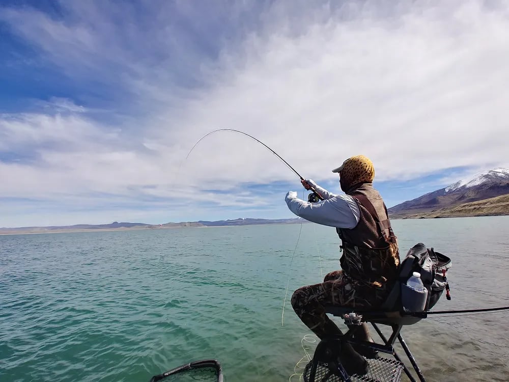 Angler casting a fly rod from a wading chair in shallow lake water
