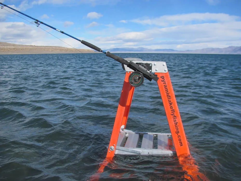 Two anglers in float tubes fishing on a calm lake with mountains in the background.