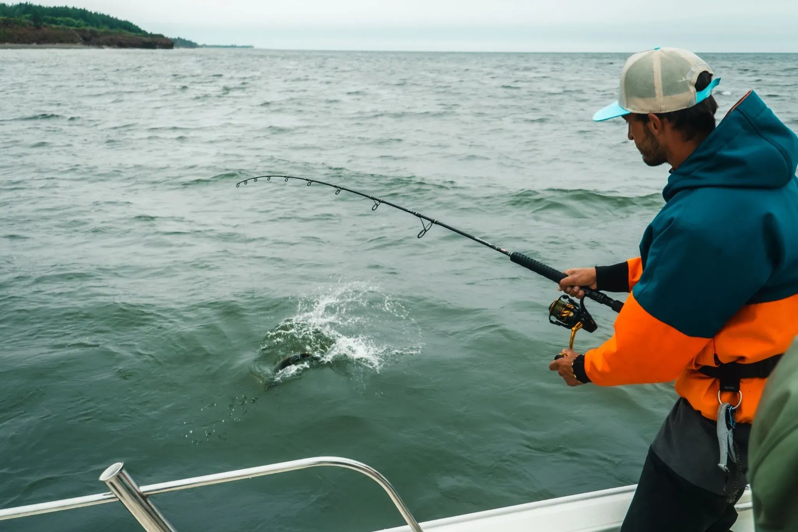 Angler fighting a fish from a white boat on choppy water.
