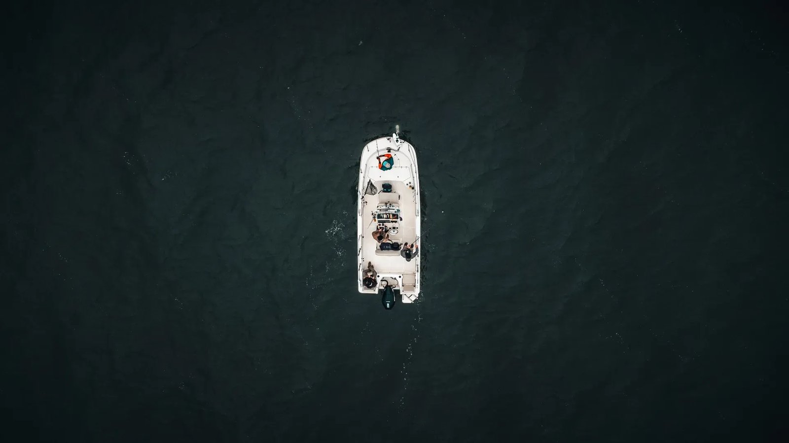 Overhead view of a white fishing boat with people on dark water.