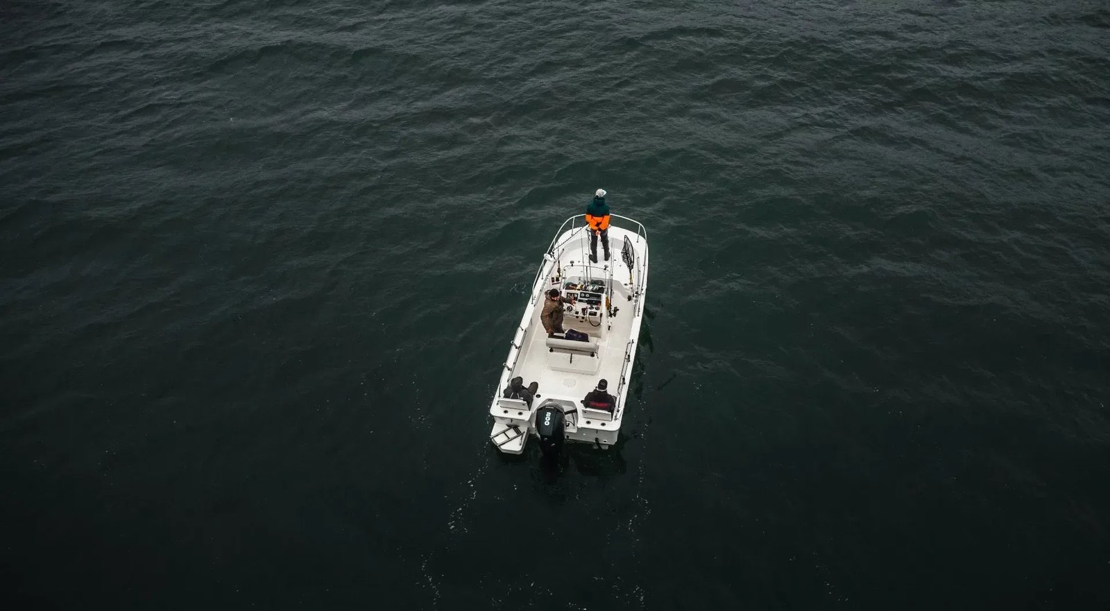 Aerial view of a white center console boat with anglers on dark water.