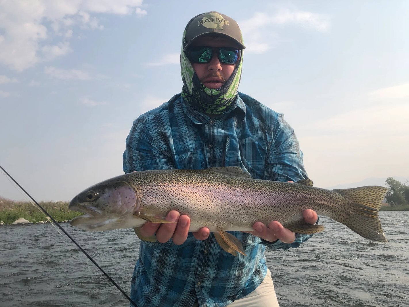 Angler in a plaid shirt holding a Steelhead in a river.