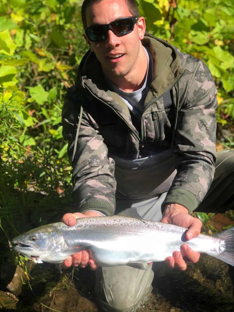 Angler in sunglasses holding a bright Silver Salmon in a river.